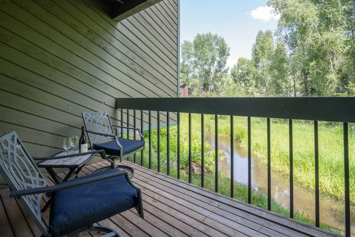 A tranquil riverside setting with two chairs and a small table positioned next to a stream, surrounded by lush greenery. The scene invites relaxation and connection with nature, ideal for unwinding after outdoor adventures.