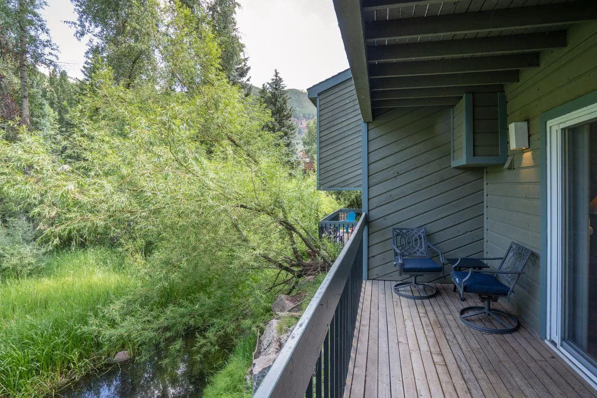 The image features a private balcony with comfortable seating overlooking lush greenery—a tranquil outdoor spot perfect for relaxing with a drink or gathering with friends and family. The view of nature reinforces the seamless indoor-outdoor living that defines a mountain town experience.