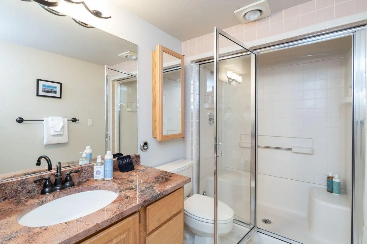 A fresh and modern guest bathroom, featuring a granite countertop, a glass-enclosed walk-in shower, wooden cabinetry for thoughtful storage, and a tastefully framed mirror. The design provides both functionality and style, enhancing the home's sense of luxury.