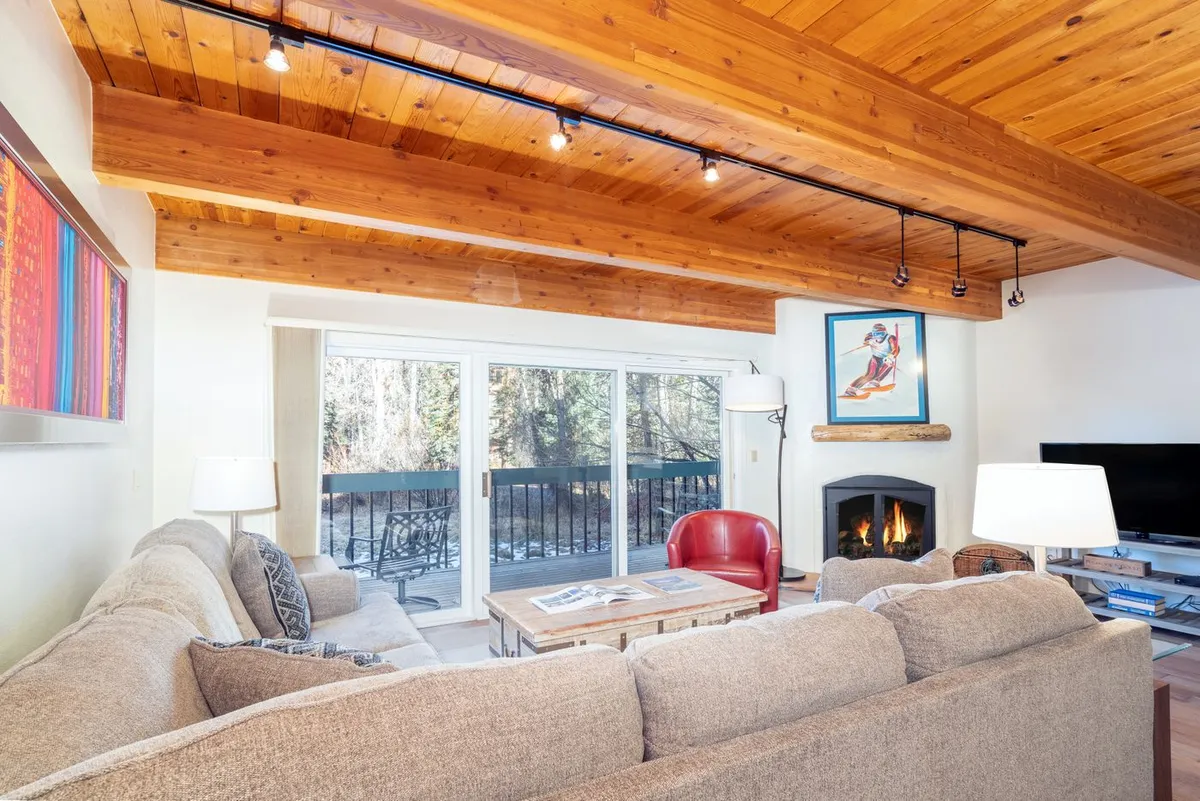 A bright and inviting living room with a plush sofa, a striking red chair, a modern fireplace, large windows flooding the space with natural light, and carefully selected artwork on the walls. The setting is perfect for relaxing, entertaining, or enjoying quiet moments by the fire.