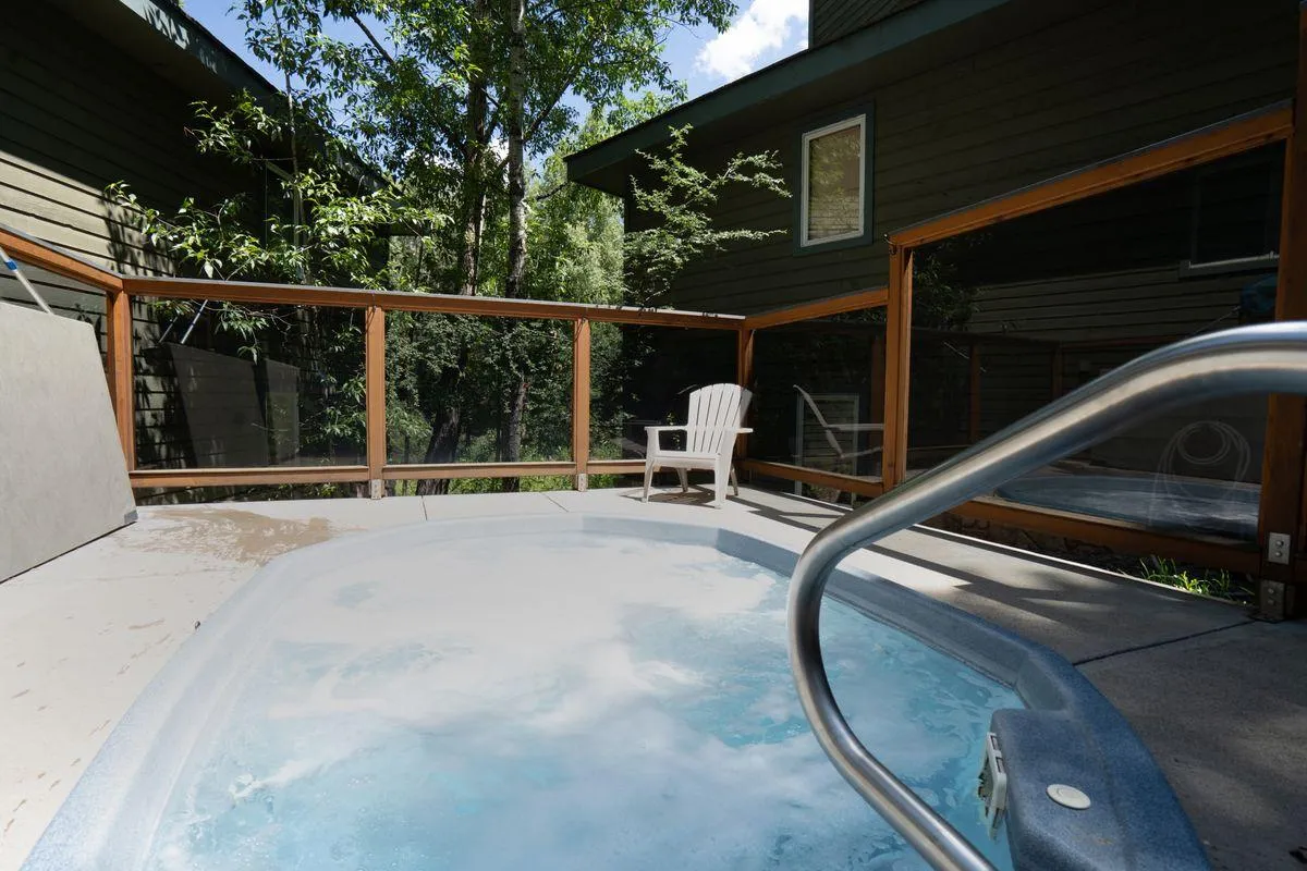 A tranquil outdoor hot tub set amidst a backdrop of leafy trees and lounge chairs, inviting guests to relax while soaking in the natural surroundings. The area looks private and serene, perfect for unwinding after a day of adventure.
